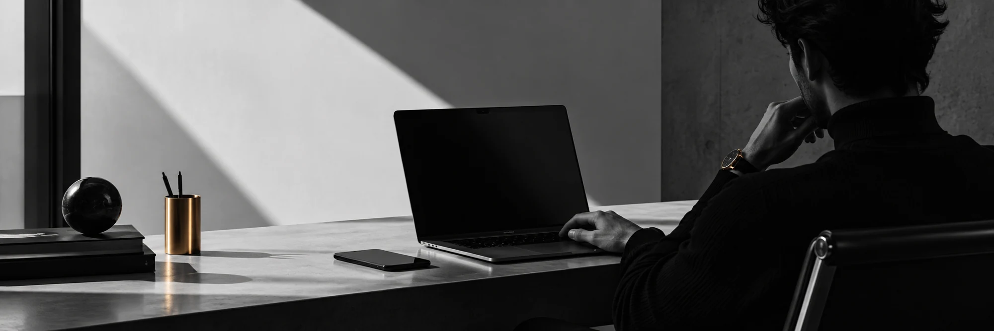 A quiet monochrome workspace with a laptop and strong afternoon light
