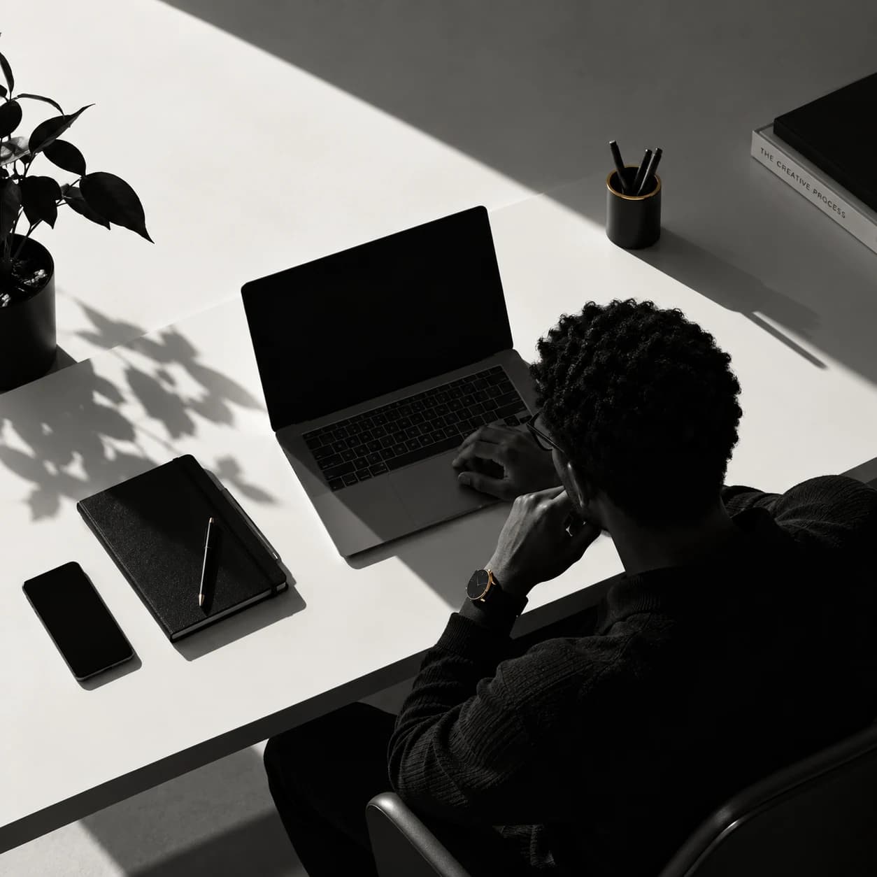 Overhead view of a minimal desk with a laptop, notebook, and geometric shadows